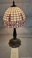 Full view of stained glass lamp with dome-shaped shade featuring pink floral designs and ornate metal base.