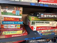 Shelf display showing stack of vintage games including Ants in the Pants, Memory, Croxley Puzzle, and others