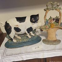 Photo showing the pig door stop with piglet and the flower basket door stop side by side on a white cloth.