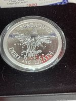 Close-up of proof silver medallion showing the design with an eagle, pyramid with eye, and inscription "SPREADING DEBT and DEATH".