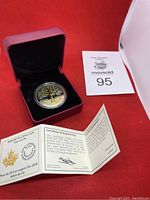 Coin in red presentation box with certificate and lot number card