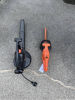 Overhead photo of electric Black and Decker leaf blower and hedge trimmer side by side on pavement.