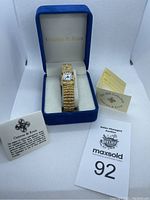 Gold tone women's watch inside blue box with collection pamphlets and auction tag visible.