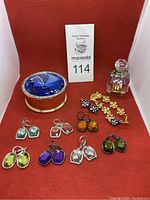 Overview photo of all jewelry items including 7 pairs of large faceted faux gemstone earrings in various colors, gold-tone blue flower bracelet and matching blue flower earrings, small clear perfume bottle, and Lori Grenier jewelry holder with a large blue gem.