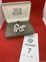 Brooch inside the original brown and cream box with Nolan Miller Ornament Collection printed on the lid.