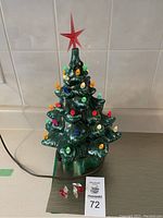Full view of ceramic Christmas tree with red star topper and colorful bulbs plugged in. Shows extra replacement bulbs below the tree.