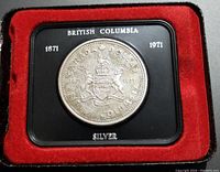 Front view of the coin in display case showing British Columbia coat of arms with inscriptions and silver marking.