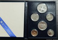 Full view of the six coin set inside the open blue display case with white cover and blue ribbon trim