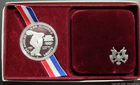Silver proof coin featuring Los Angeles XXIII Olympiad design with discus thrower, in original red velvet case with ribbon and eagle pin.