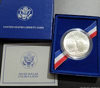 Image of sealed 1986 US silver commemorative dollar coin in original blue presentation box with accompanying certificate.