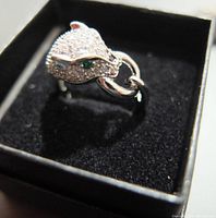 Front side close-up of sterling silver leopard head ring with clear and green gemstones in a black ring box.