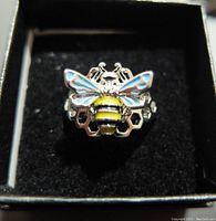 Top front view of the 925 stamped silver ring featuring a bee with enamel decorated wings and yellow/black striped body on a honeycomb base.