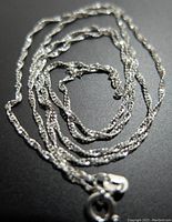 Photo of the silver twisted rope necklace chain showing the clasp and texture of the chain links on a dark background.