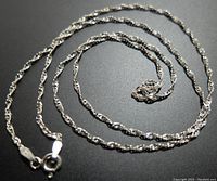 Full view of the twisted rope style silver necklace coiled on a flat surface, highlighting the entire length and chain design.