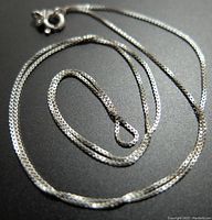 Close-up image of the silver box chain necklace laid out, showing the chain links, clasp, and length.