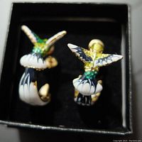 Pair of hummingbird earrings in a box, showing front design with colorful green, white, black enamel on gold-tone metal.