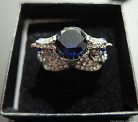 Top view of the silver ring showing a large round deep blue gemstone surrounded by clear and blue accent stones.