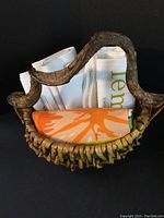 Handmade woven basket holding rolled dish towels in white and orange with green print on a black background