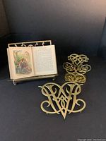 Lot showing the brass folding book holder displaying an open illustrated book, The Pilgrim's Progress, along with two brass cypher bookends with intricate design.