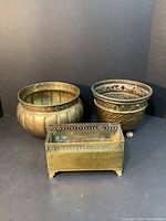 Three brass planters shown together, two round and one rectangular, highlighting differing styles and sizes