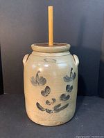 Full view of the butter churn crock with wooden plunger showing the body, floral design, and handles.