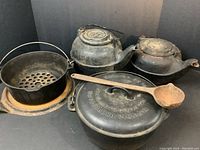 Full set of cast iron cookware items arranged together including Dutch ovens, kettles, trivet, and ladle