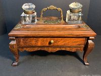 Front view of oak stationery box with brass handle, drawer closed, cut glass ink wells on top.