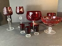 Full view of cranberry glass collection including 2 stem wine glasses with etched design, a cranberry bowl, 4 small aperitif glasses, candy dish, and jar.
