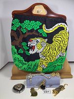 Full view of vintage beaded tiger sewing bag with green foliage, brooches, keychain, compact mirror and earrings displayed on stand.