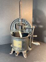 Full view of the manual press showing the overall shape, cast iron build, embossed manufacturer name, crank handle and round base with drainage spout.