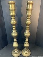 Front view showing two tall brass candlesticks with rounded and turned design including hand carved detailing on the surface.