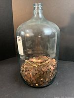 Full view of large clear glass Belmont Springs water bottle containing pennies about halfway up.