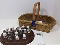 Photo showing the sewing basket and 19 assorted collector thimbles displayed on a wooden board.