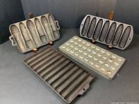 Four vintage cast baking forms displayed on black surface: three cast iron cornbread pans and one cast steel chocolate mold.