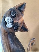 Close-up of one hand-carved and painted wooden cat figurine with tilted head and detailed facial features.