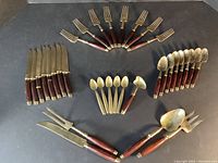 Full overview of the vintage wood and brass flatware set arranged on a black surface, including knives, forks, spoons, and serving utensils.