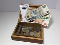 Open wood box showing rolled US pennies, assorted coins, and Singapore bills including $1, $5, and $10 denominations