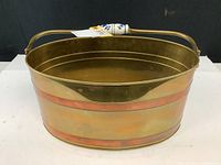 Side view of the oval brass bucket showing painted porcelain handle and copper banding.