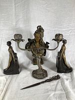 Front view of all five pieces: two-arm nymph candelabra centered with matching flower-shaped candle holders, pair of female figure bookends on each side, signed bust placed behind candelabra, and female figure letter opener in front.