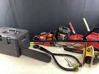 Photo showing three chainsaws, a black toolbox, bar chain oil container, fuel containers, and a haul chain.