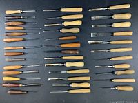 Overhead view of 38 wooden-handled chisels arranged in rows on black background
