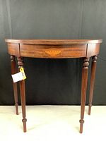Front view of the demilune occasional table showing the urn inlay detail and fluted legs.