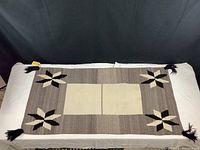 Full view of Navajo weaving rug with star motifs and central cream rectangles against grey background. Rug laid on white surface with black backdrop.