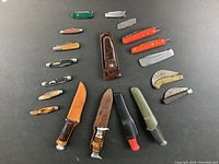 Overview of the 19 knives including fixed and folding blades with sheaths arranged on table