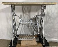 Front view of Singer wrought iron sewing table base with spray painted silver finish and unattached Formica top.