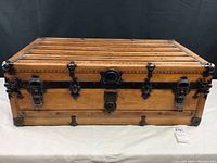 Front view of wooden steamer trunk showing metal latches and lock, leather wrapped corners, and riveted metal reinforcements