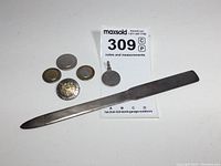 Photo showing entire lot with letter opener, pendant, US Coast Guard lapel pin, and coins for scale.