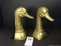 Front view of the pair of brass duck head bookends, showing detailed facial features and flat base plate.