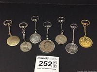 Full view of seven vintage coin and medallion key chains arranged in a line, showing size and design variety.