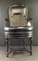 Full front view of chair showing leather upholstered seat, caned back, and carved wooden frame.